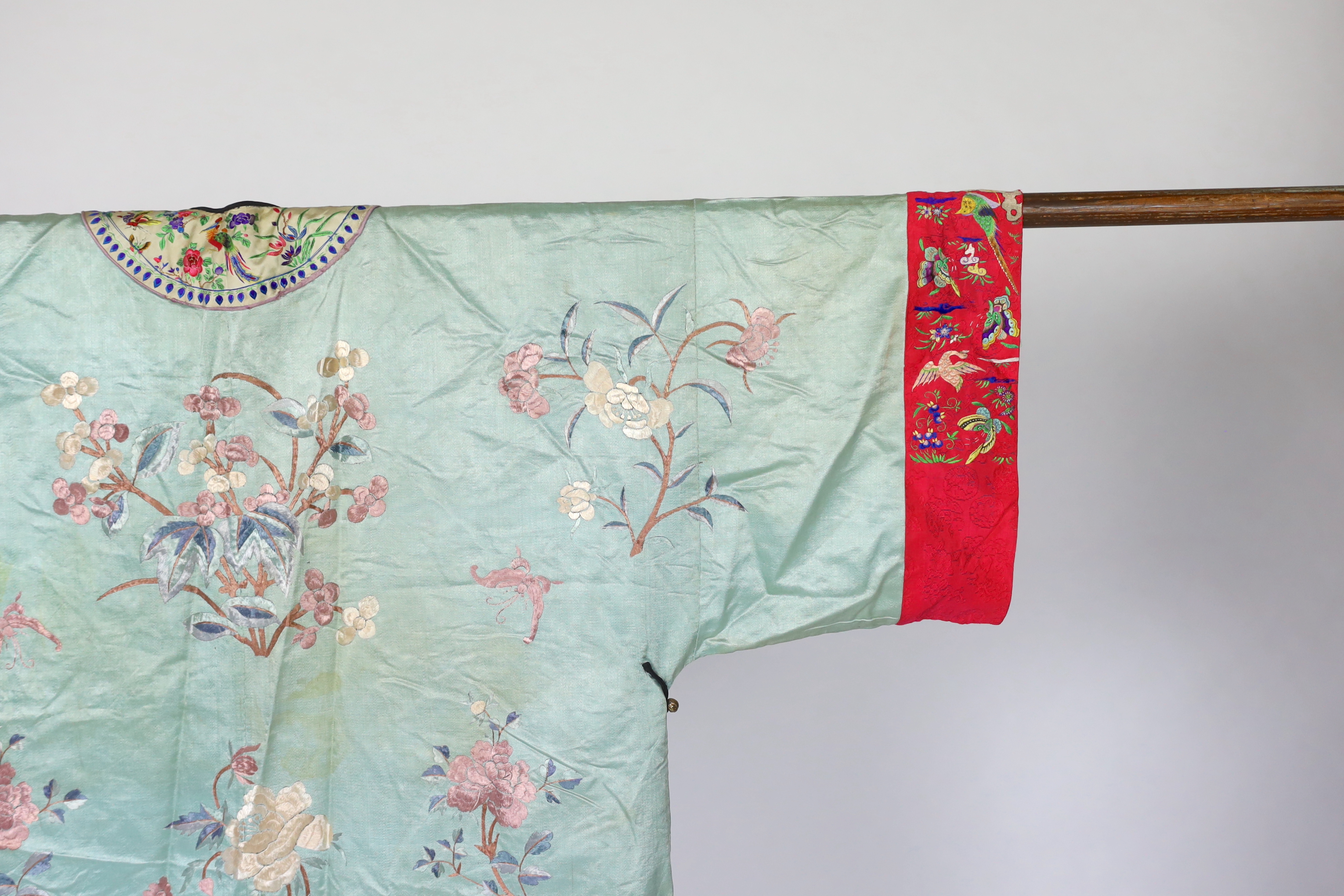 An early 20th century Chinese silk embroidered turquoise robe, embroidered in pastel silk with butterflies and flowers all over, polychrome embroidered braiding edged with lilac and bright pink sleeve bands embroidered w